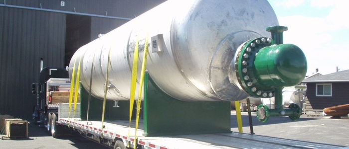 Completed stainless steel vessel with flanged nozzles strapped to a flatbed trailer