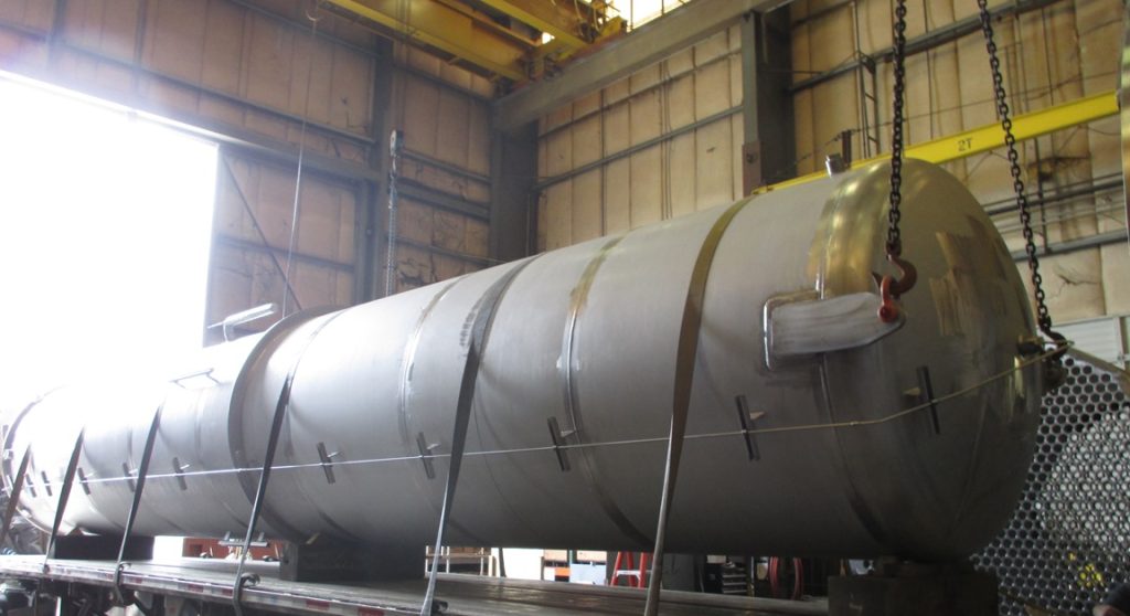 Large fabricated vessel being loaded onto a trailer by overhead crane in the Harris Thermal shop