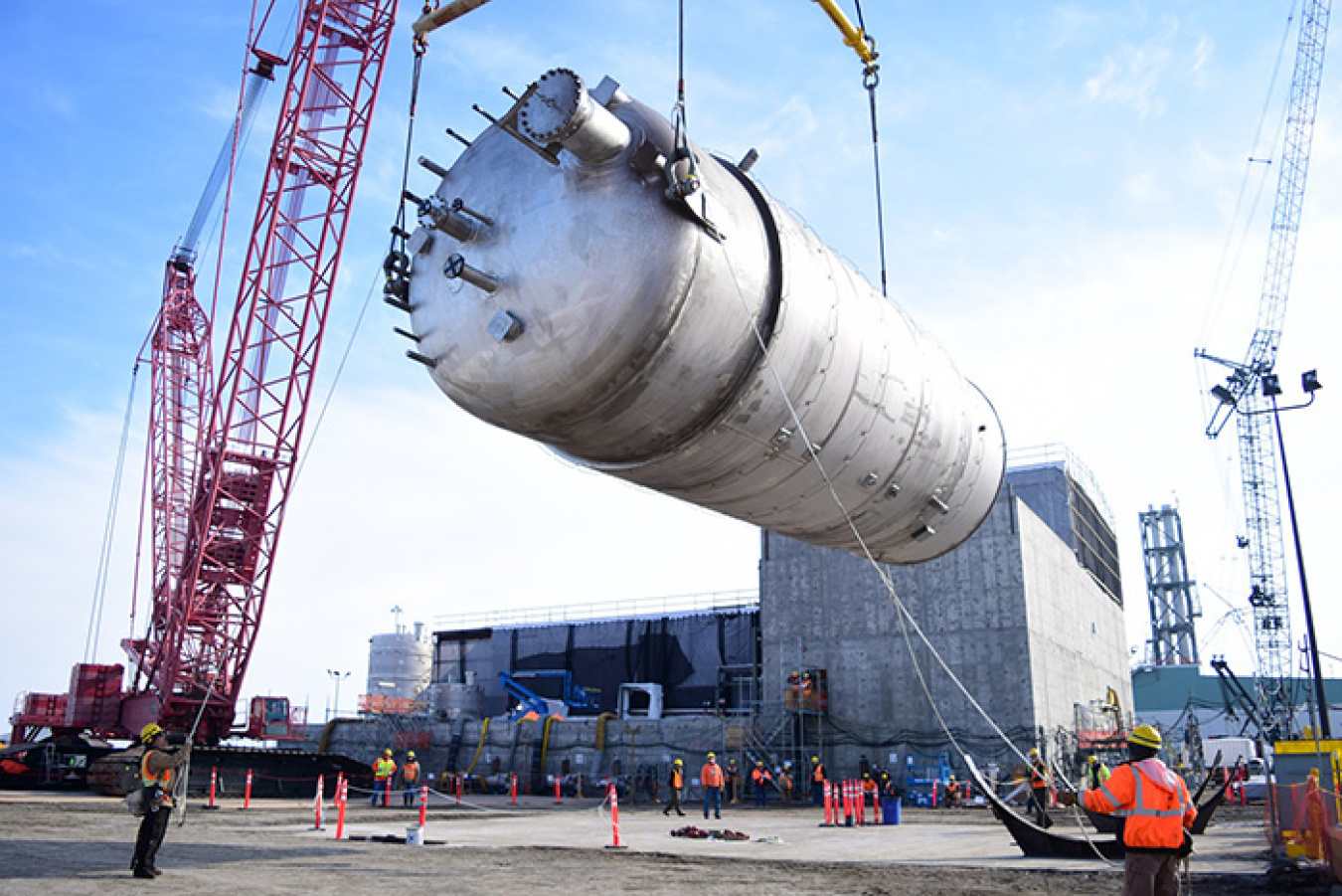A mobile crane lifting a stainless steel vessel into a fabrication facility